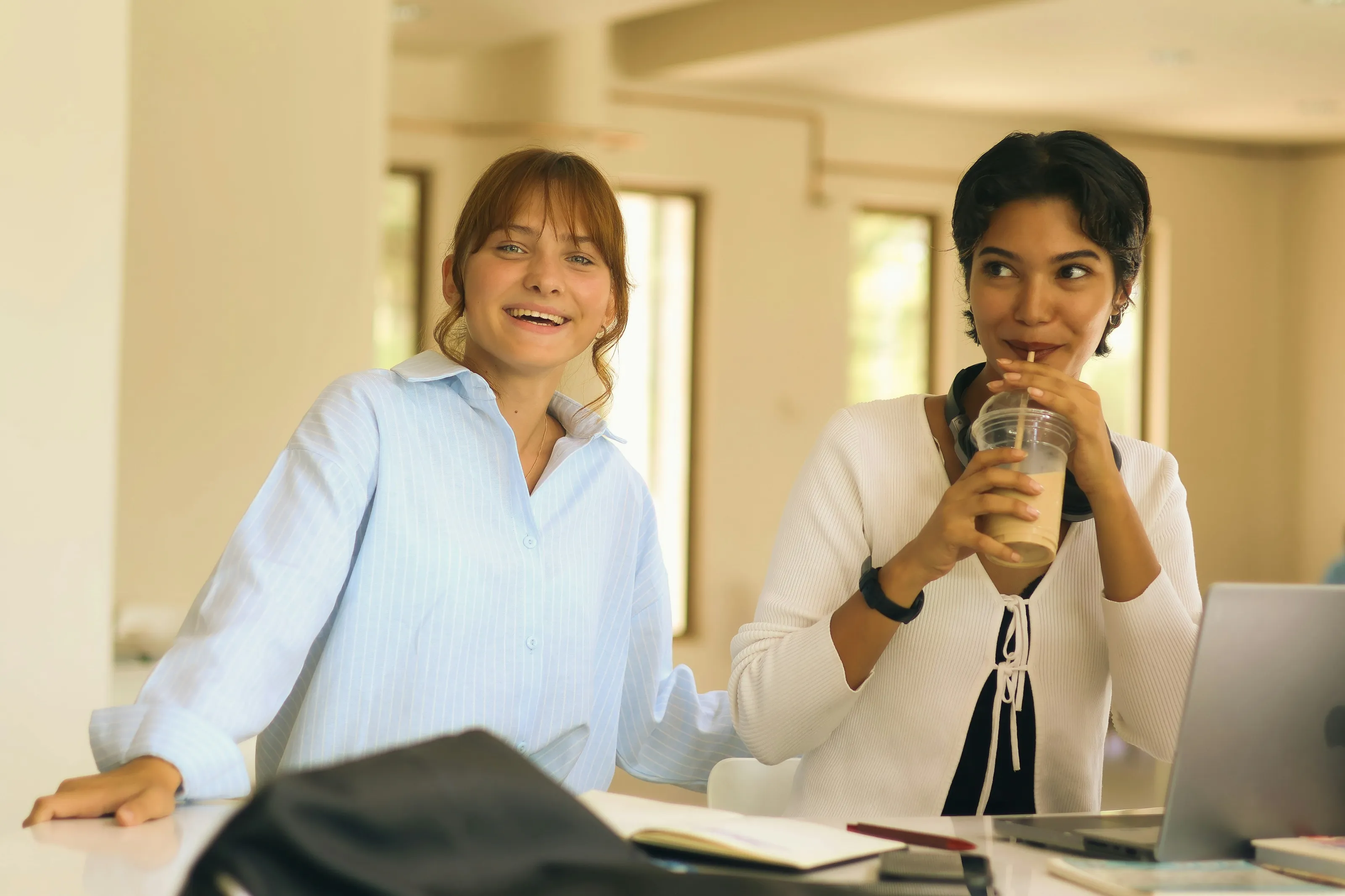 Two women laughing together over coffee at a work table
